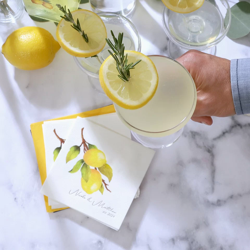 Hand holding a limoncello martini. A custom cocktail napkin with a lemon on it in the background 
