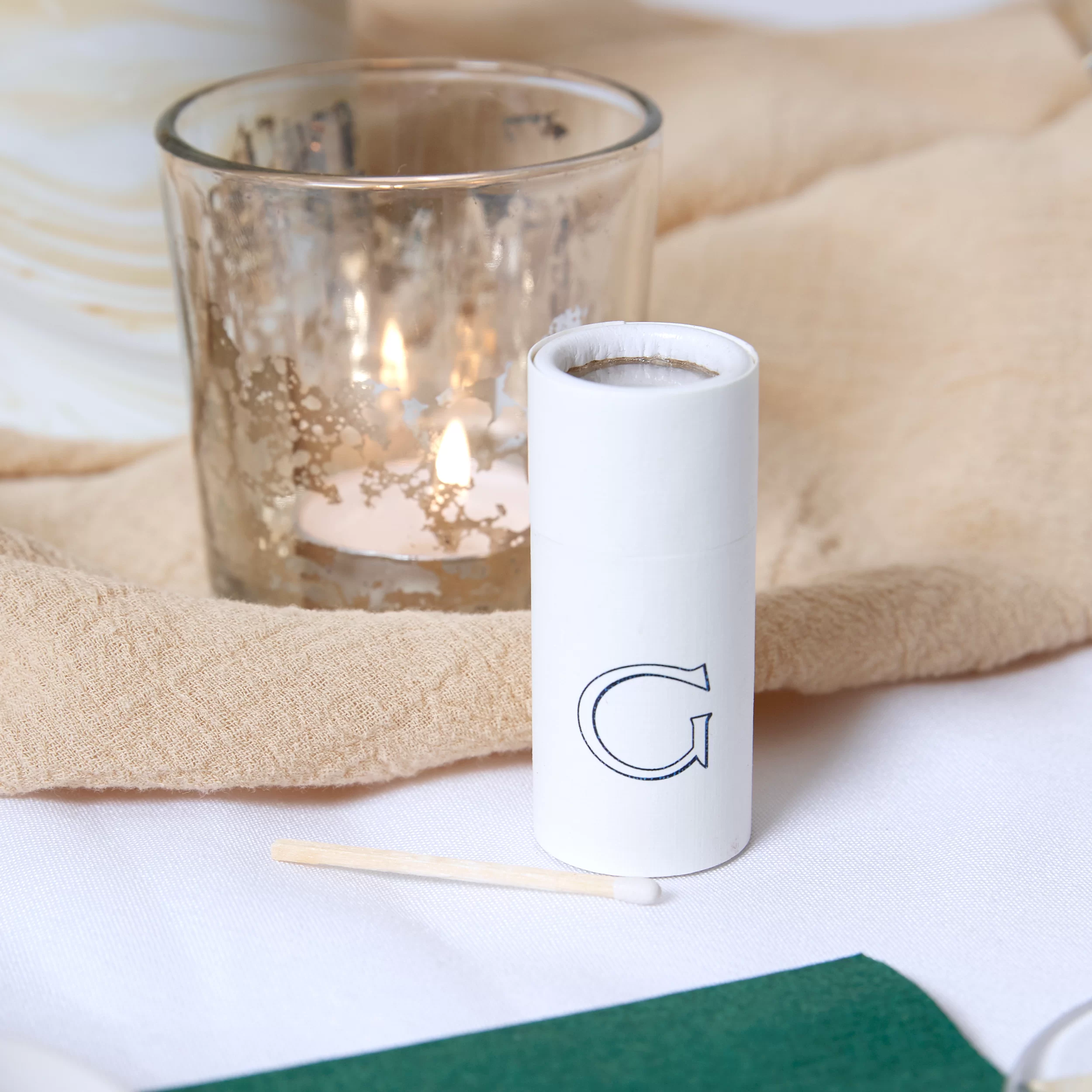 Barrel Matchbox in front of a candle with the letter G printed on the matchbox