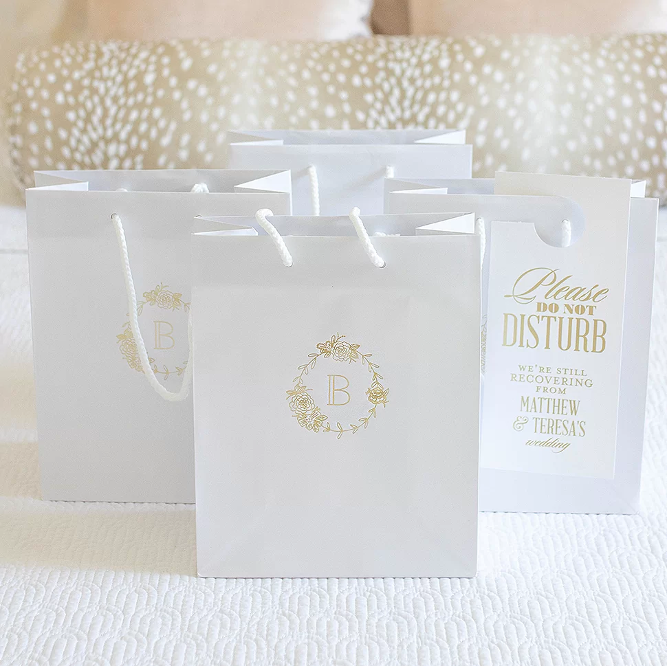 Classic Gift Bags printed with peony wreath and initial shown on a bed