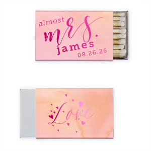 The Excitement Ignites! Celebrate the bride-to-be with the Almost Mrs. Matchbox. Featuring a dramatic "almost Mrs." script on the front and "Love" surrounded by floating hearts on the back, this vibrant design captures the rising excitement as the big day approaches. Perfect for wedding showers and bachelorette parties!