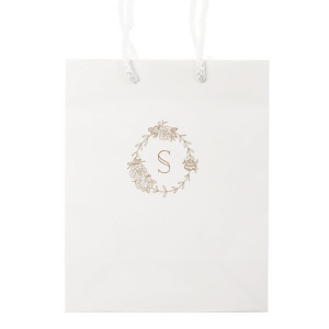 The Romantic Peony Frame Monogram Bag elegantly captures the essence of joy and romance. A wreath of lush peonies and greenery forms a delicate frame, encircling the celebrant's initial in a graceful display. This design exudes elegance, symbolizing happiness, prosperity, and a blissful union.