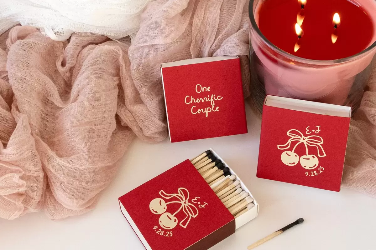 3 Large Red Matchboxes next to a lit candle with a cherry graphic on them 